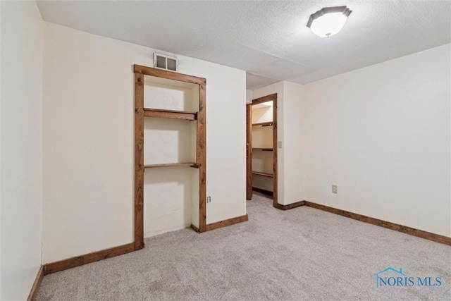 unfurnished bedroom with a walk in closet, a closet, light carpet, and a textured ceiling