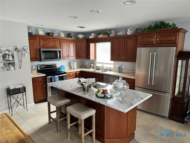 kitchen with appliances with stainless steel finishes, a kitchen breakfast bar, a center island, light tile patterned floors, and sink