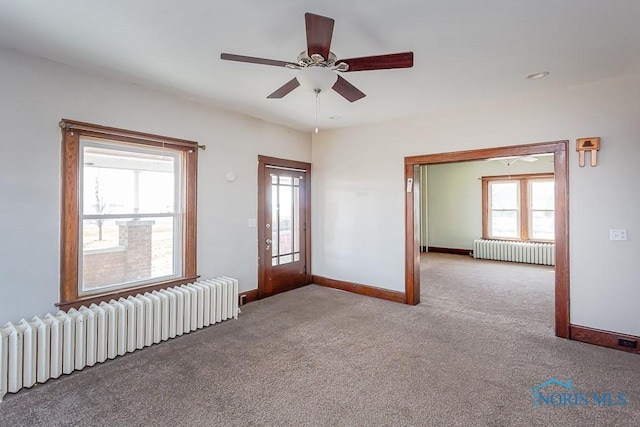 carpeted empty room with radiator heating unit, a ceiling fan, and baseboards