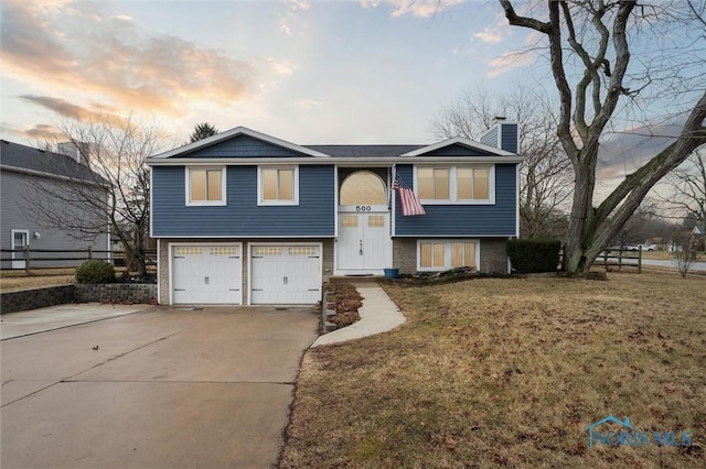 bi-level home featuring a garage, driveway, a front lawn, and a chimney