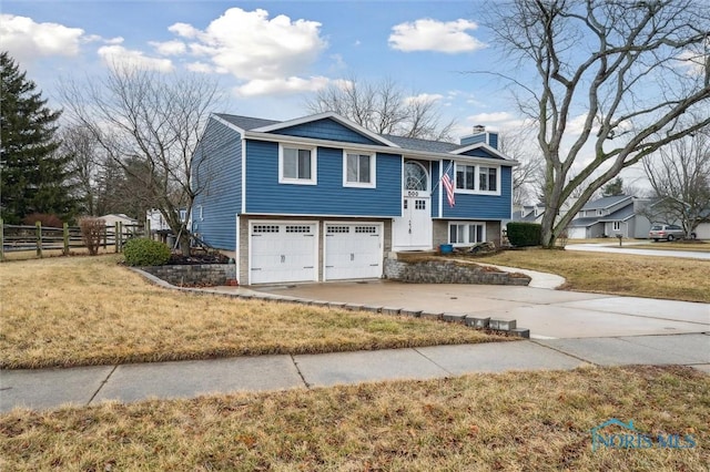 split foyer home featuring an attached garage, fence, concrete driveway, a front lawn, and a chimney