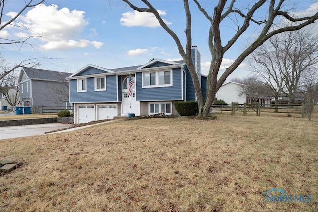 bi-level home featuring a garage, a chimney, a front yard, and fence