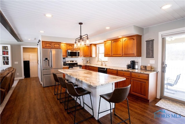 kitchen with hanging light fixtures, a kitchen island, tasteful backsplash, appliances with stainless steel finishes, and a kitchen breakfast bar