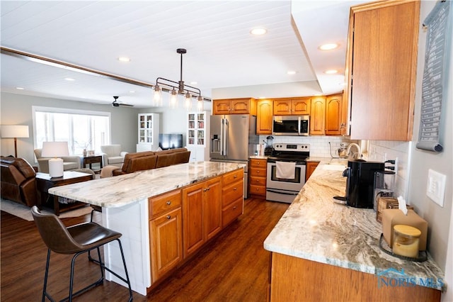 kitchen with appliances with stainless steel finishes, a breakfast bar area, dark wood-type flooring, a center island, and backsplash