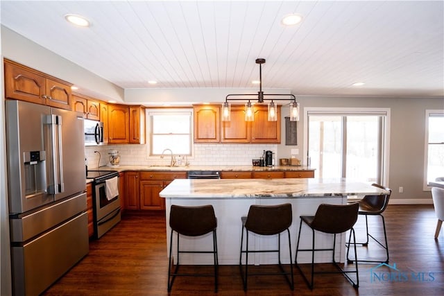 kitchen with decorative light fixtures, a kitchen island, sink, tasteful backsplash, and appliances with stainless steel finishes