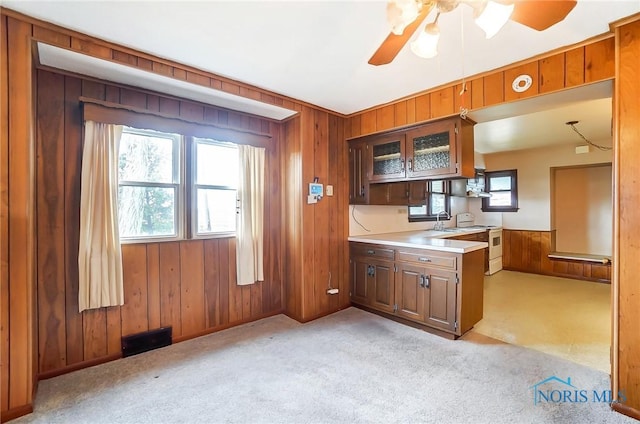 kitchen with wooden walls, white electric stove, ceiling fan, sink, and light colored carpet