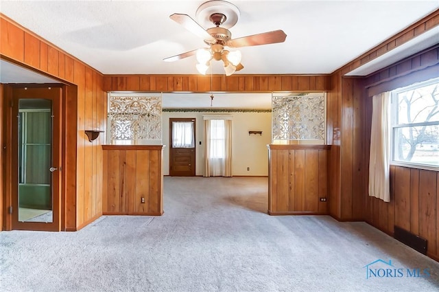 interior space with light carpet, wooden walls, and plenty of natural light