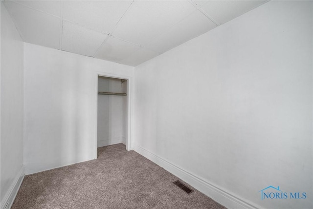 unfurnished bedroom featuring carpet floors, a closet, and a paneled ceiling