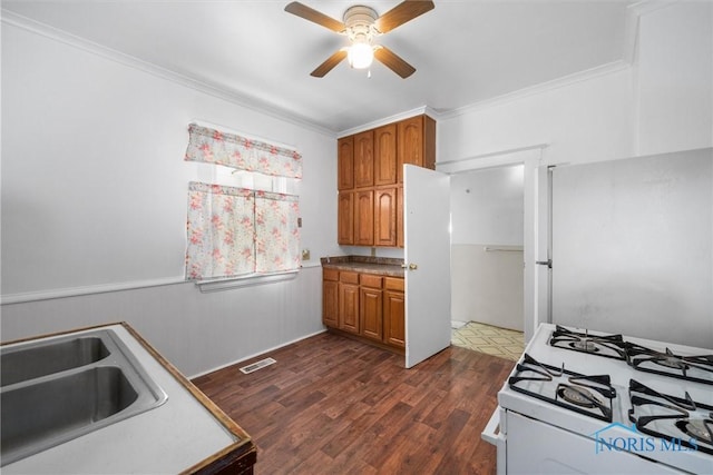 kitchen featuring refrigerator, sink, white gas stove, dark wood-type flooring, and crown molding