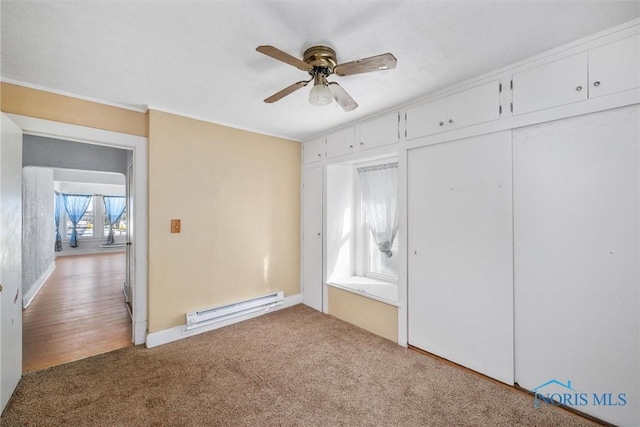 unfurnished bedroom with baseboard heating, ceiling fan, carpet flooring, and a closet