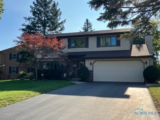 traditional-style house with a garage, driveway, a chimney, and a front yard