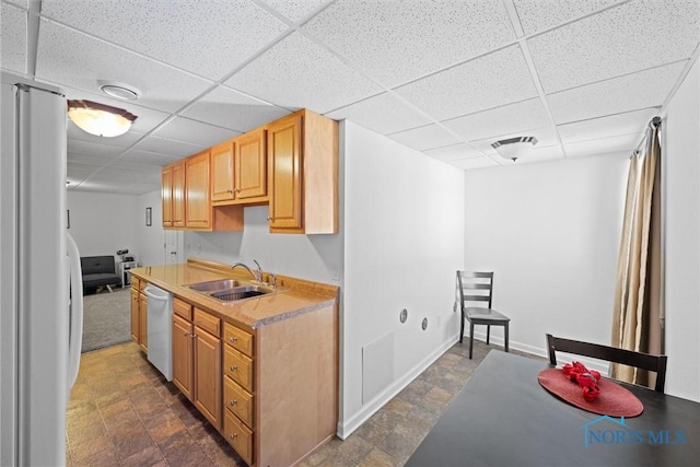 kitchen with a paneled ceiling, white appliances, a sink, light countertops, and stone finish floor