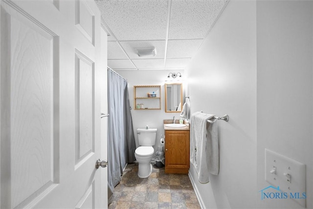 full bathroom featuring curtained shower, a drop ceiling, toilet, vanity, and stone finish floor