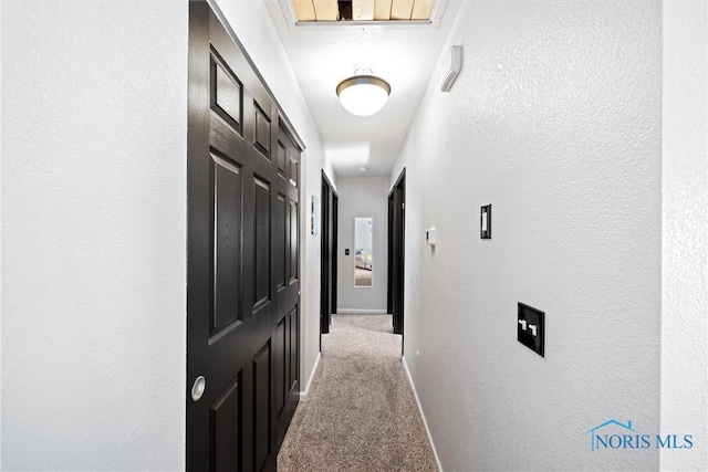 hall with light colored carpet, a textured wall, and baseboards