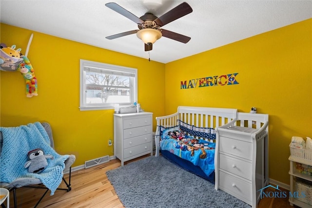 bedroom with ceiling fan, wood finished floors, visible vents, and baseboards