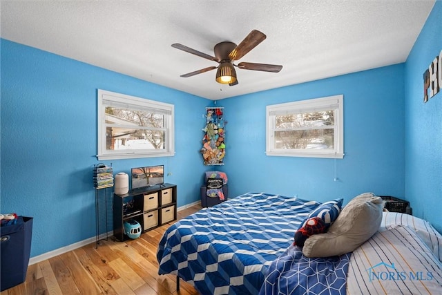 bedroom with a textured ceiling, wood finished floors, a ceiling fan, and baseboards