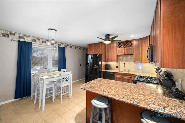 kitchen featuring a peninsula, a sink, backsplash, brown cabinets, and black appliances