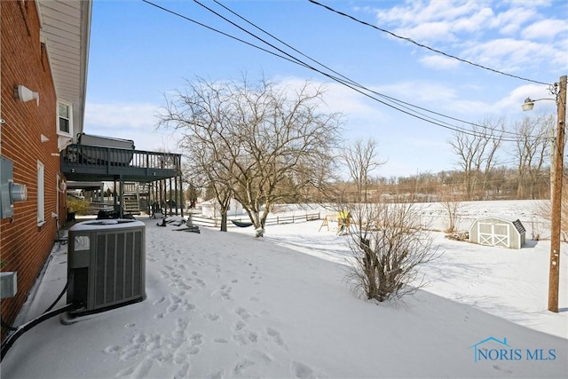 snowy yard with a deck, central AC unit, an outdoor structure, stairway, and a shed