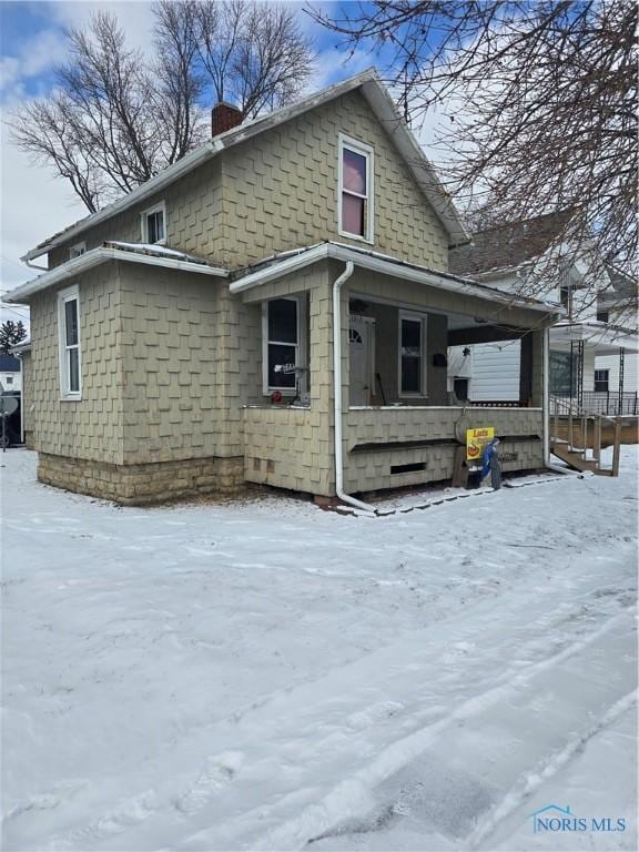 snow covered property featuring covered porch and a chimney