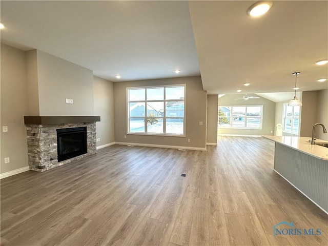 unfurnished living room with a fireplace, sink, light wood-type flooring, and a healthy amount of sunlight