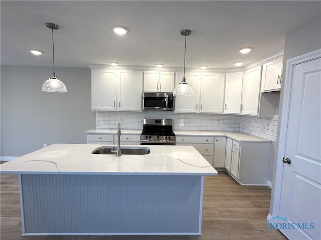 kitchen featuring appliances with stainless steel finishes, white cabinets, light stone counters, and pendant lighting