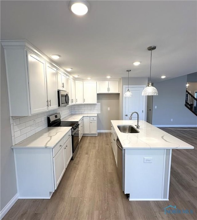 kitchen featuring a center island with sink, stainless steel appliances, light stone counters, sink, and white cabinetry