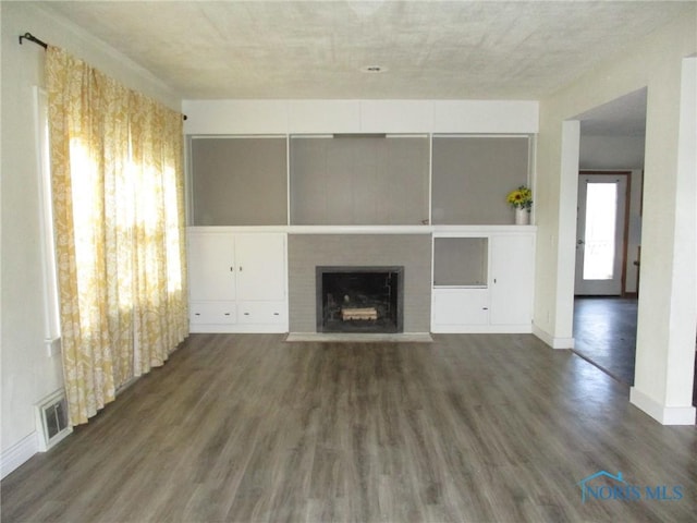 unfurnished living room with a fireplace with flush hearth, visible vents, baseboards, and wood finished floors