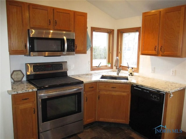 kitchen with a sink, vaulted ceiling, appliances with stainless steel finishes, decorative backsplash, and brown cabinetry