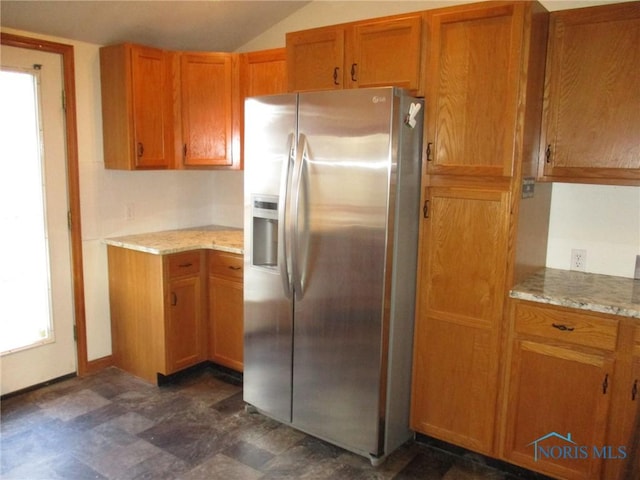 kitchen with lofted ceiling, light stone counters, brown cabinetry, and stainless steel fridge with ice dispenser