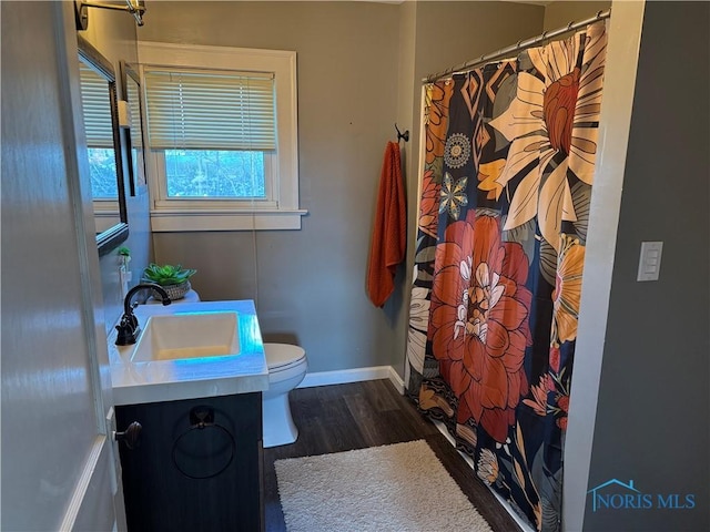 bathroom with curtained shower, toilet, vanity, wood finished floors, and baseboards