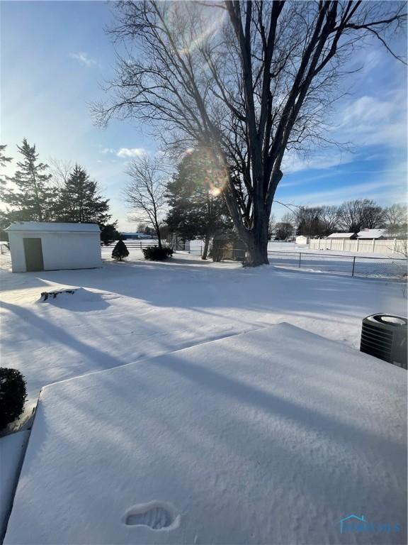 snowy yard featuring central AC unit, a garage, and an outdoor structure