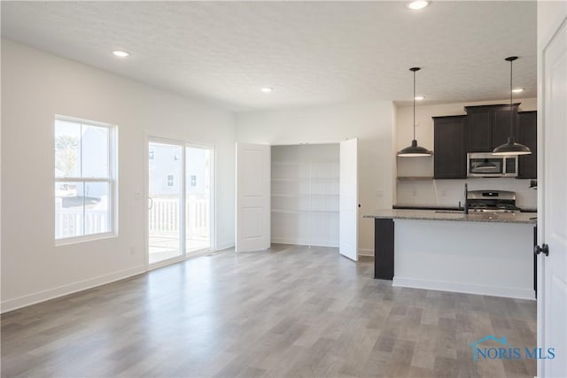 kitchen with stainless steel appliances, light stone countertops, a textured ceiling, pendant lighting, and hardwood / wood-style floors