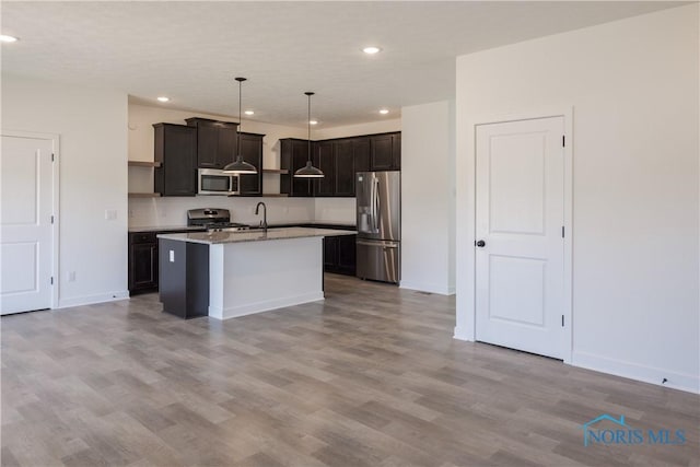 kitchen featuring light wood-type flooring, a center island with sink, sink, appliances with stainless steel finishes, and pendant lighting