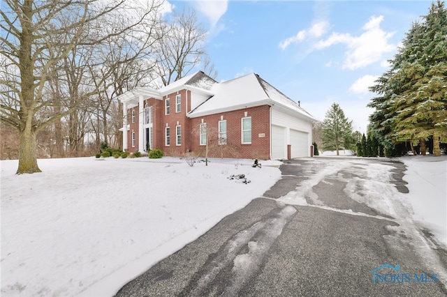 view of snowy exterior featuring aphalt driveway, brick siding, and an attached garage