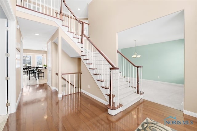 staircase featuring baseboards, a notable chandelier, wood finished floors, and a towering ceiling