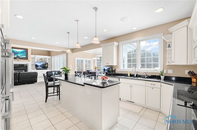 kitchen with dark countertops, a kitchen island, white cabinetry, and a sink