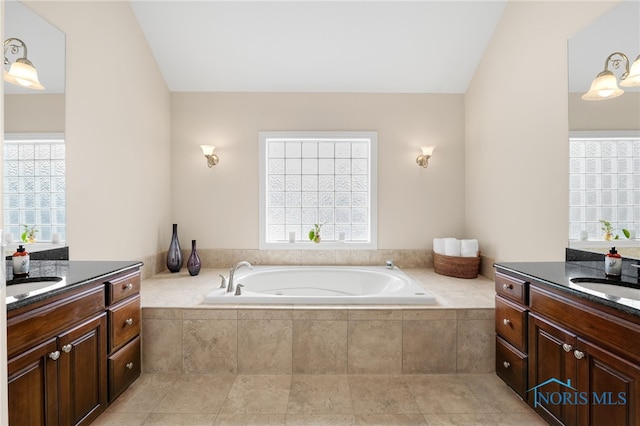 bathroom with two vanities, a bath, a healthy amount of sunlight, and a sink