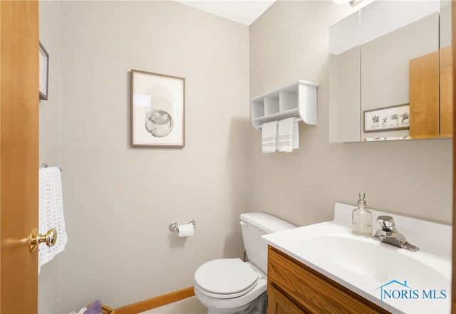 half bathroom featuring toilet, baseboards, and vanity