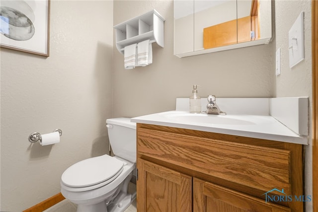 half bathroom featuring toilet, baseboards, and vanity