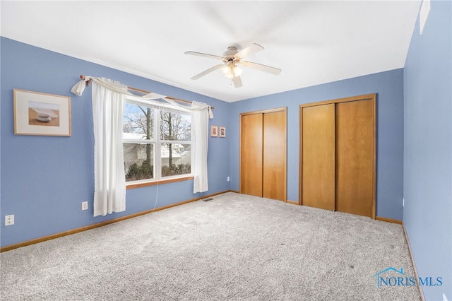 unfurnished bedroom featuring baseboards, a ceiling fan, two closets, and carpet flooring