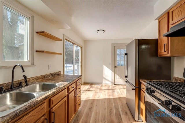 kitchen featuring sink, a textured ceiling, stainless steel gas range oven, and light wood-type flooring