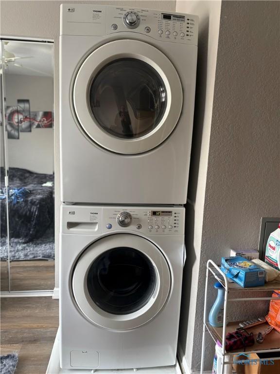 clothes washing area featuring a textured wall, laundry area, dark wood-type flooring, and stacked washer and clothes dryer