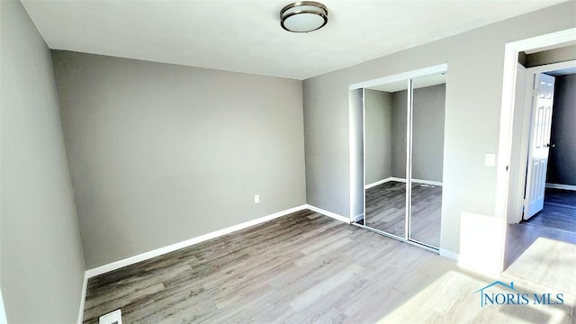 unfurnished bedroom featuring a closet, baseboards, and wood finished floors