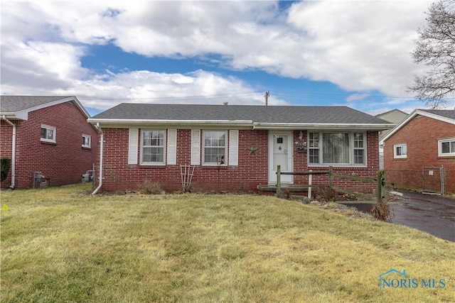 view of front of home featuring brick siding, roof with shingles, and a front yard