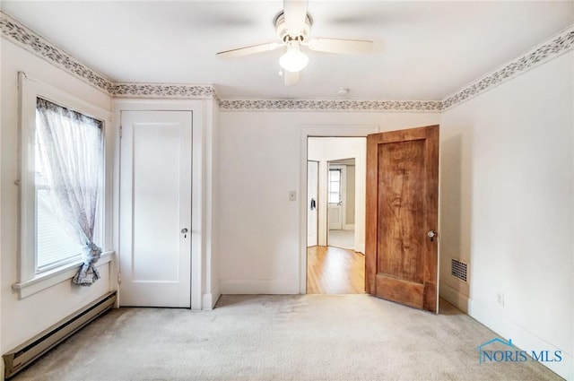 unfurnished bedroom featuring a baseboard heating unit, visible vents, multiple windows, and light carpet