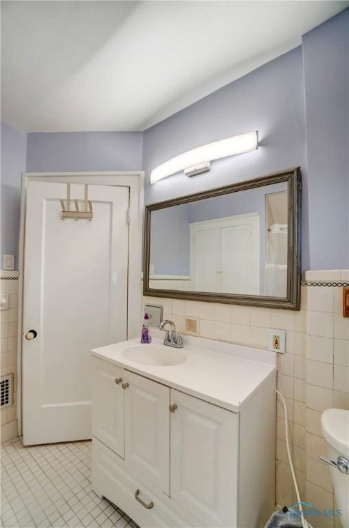 bathroom with wainscoting, toilet, tile patterned floors, vanity, and tile walls