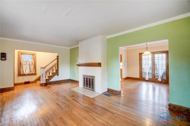 unfurnished living room with light wood-type flooring, a brick fireplace, visible vents, and stairway