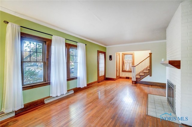 unfurnished living room featuring crown molding, light wood finished floors, a baseboard radiator, stairway, and a brick fireplace