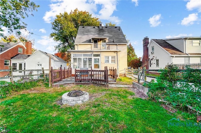 rear view of property featuring a yard, an outdoor fire pit, a balcony, a fenced backyard, and a wooden deck