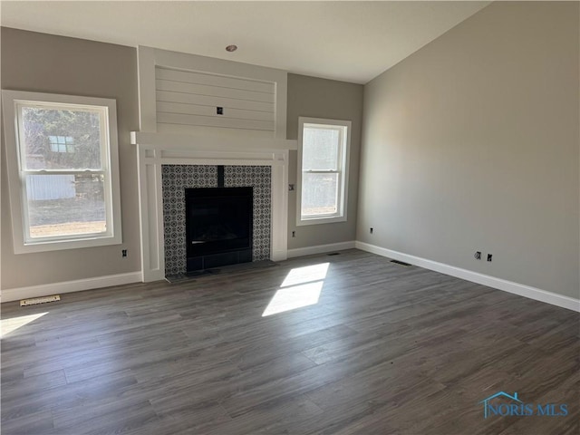 unfurnished living room with dark wood finished floors, visible vents, a fireplace, and baseboards